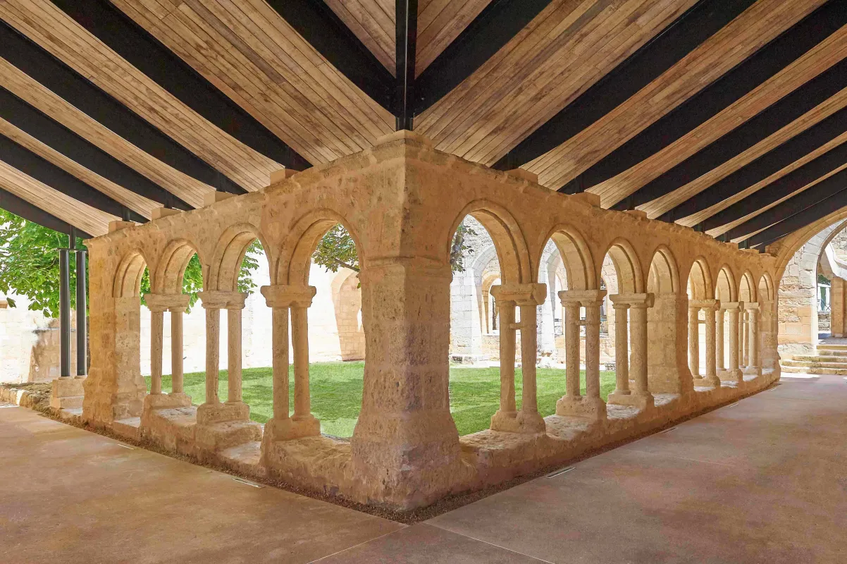 Cloître roman médiéval avec colonnes en pierre et arcades cintrées sous un plafond en bois moderne, illustrant l'architecture historique de Saint-Emilion.