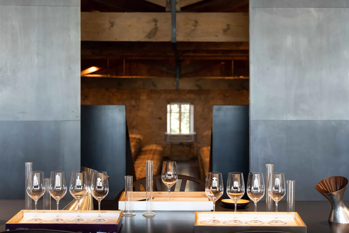 Salle de dégustation du Château de Ferrand avec des verres à vin disposés élégamment sur des tables, poutres en bois apparentes, murs en pierre, et lumière naturelle provenant d'une fenêtre en arrière-plan.