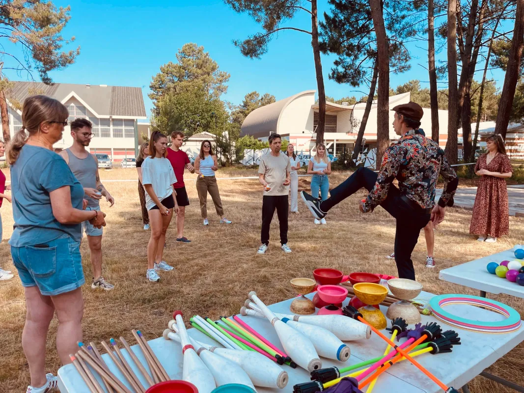 Un groupe de jeunes adultes participant à des jeux et activités d'équipe en plein air dans un parc avec des accessoires colorés et du matériel sportif exposés sur des tables, sous un ciel bleu dégagé.