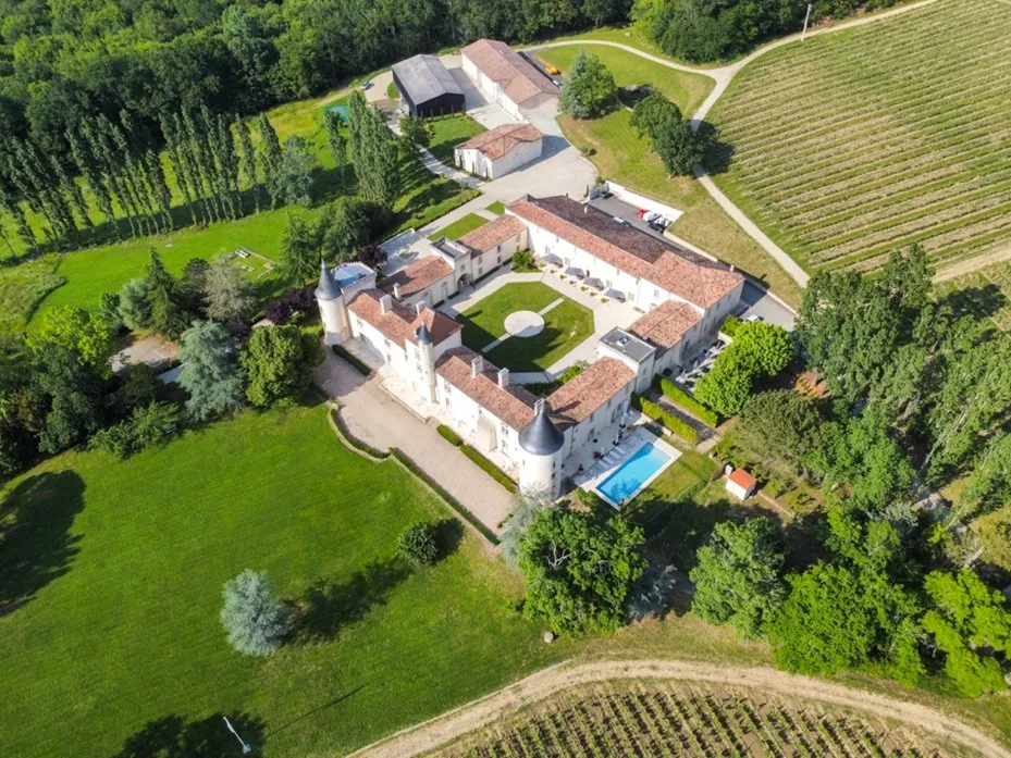 Vue aérienne du Château Toulouse-Lautrec, un château blanc historique aux toitures de tuiles terracotta, entouré de jardins aménagés, piscine et campagne verdoyante près de Bordeaux.
