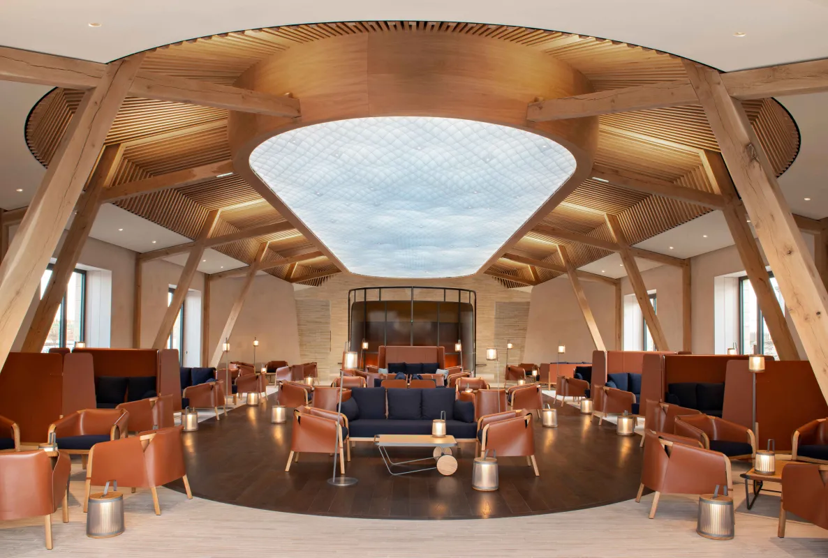Salle d'événement haut de gamme avec structure architecturale en bois, grande verrière, sièges en cuir terracotta et scène centrale au Château de Ferrand