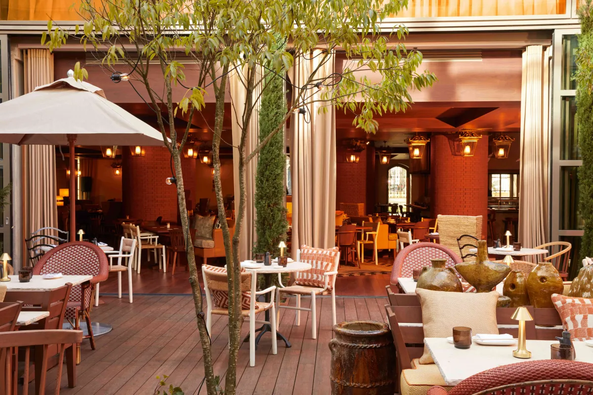 Terrasse extérieure d'un restaurant d'hôtel de luxe aux tons terracotta chauds, avec mobilier confortable, plantes décoratives et éclairage tamisé