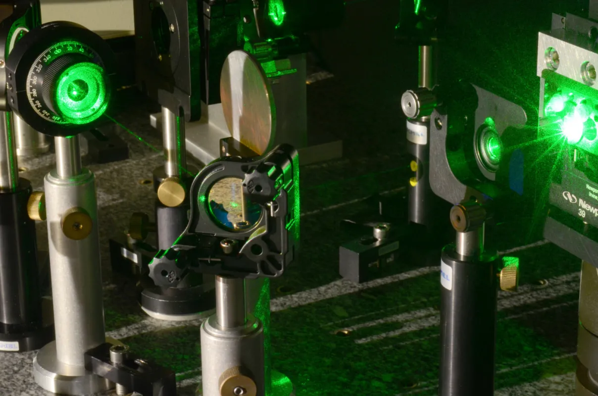 Configuration de laboratoire d'optique laser avancée avec faisceaux laser verts, composants optiques montés sur des supports ajustables et instruments de mesure de précision sur une table en granit