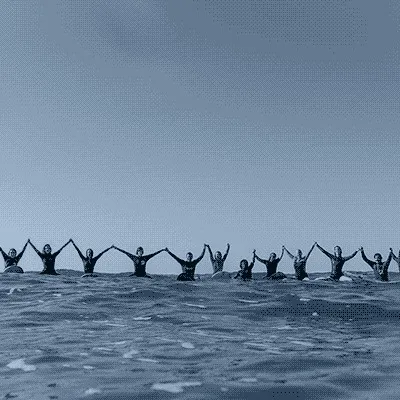 Groupe de surfeurs debout dans l'océan avec les bras levés, alignés dans l'eau peu profonde avec leurs planches