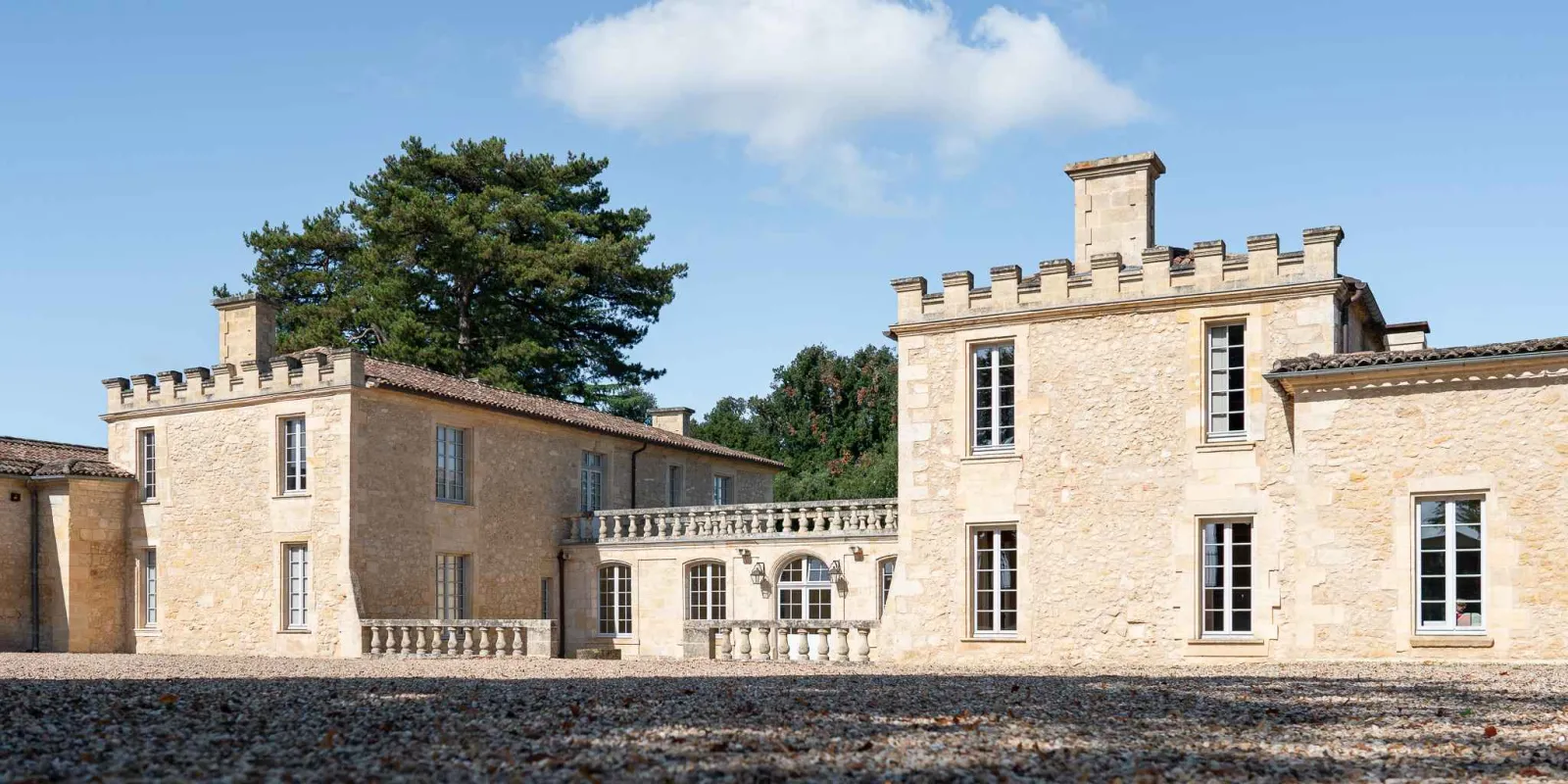 Château de Ferrand, demeure en pierre aux tours crénelées et grandes fenêtres, entouré d'une cour en gravier sous un ciel bleu dégagé près de Saint-Émilion à Bordeaux.
