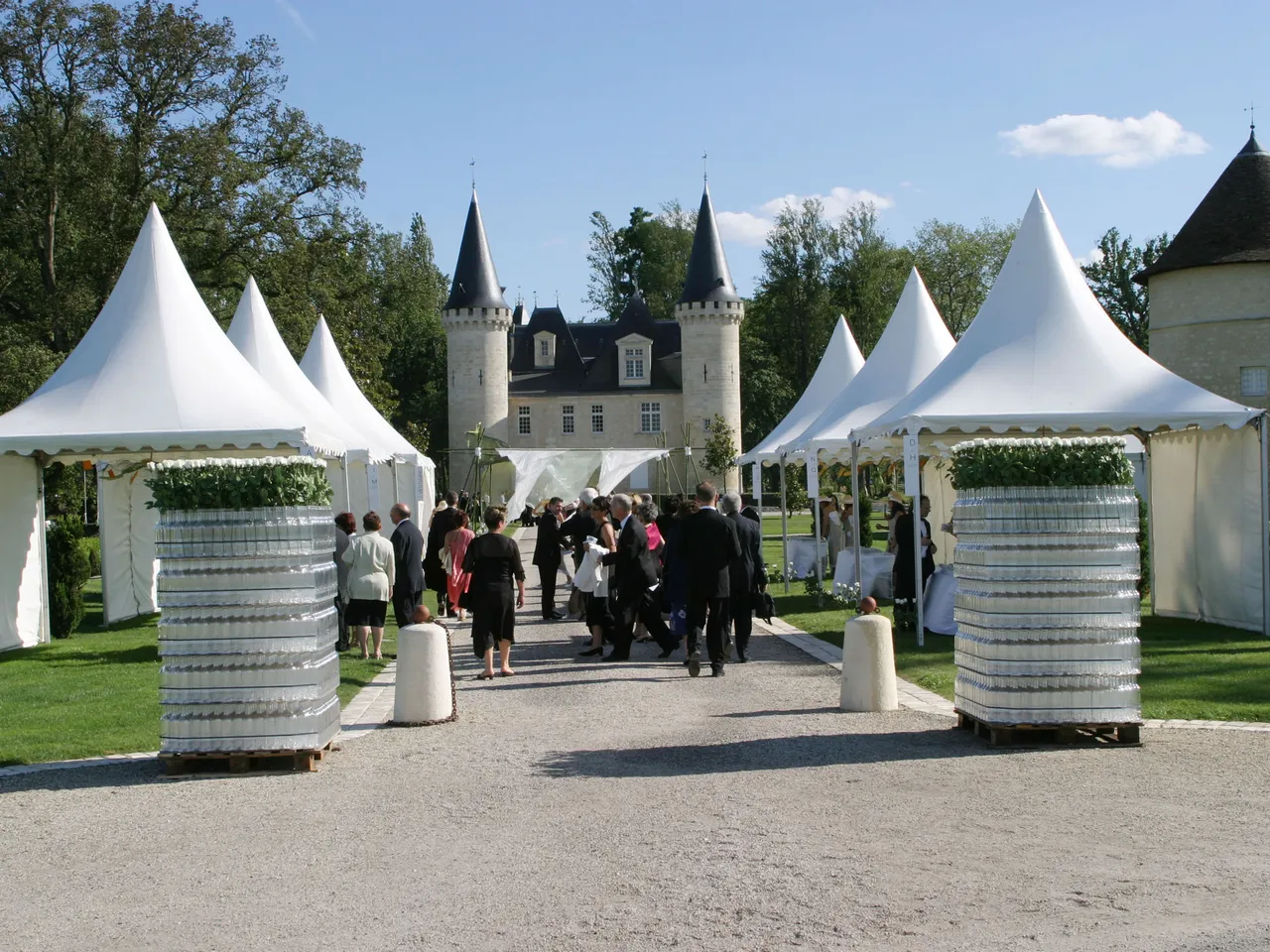 Lieu d'événement en plein air au Château d'Agassac à Bordeaux, avec des chapiteaux blancs décorés de colonnes ornées de lierre, des invités en tenue formelle, et les tours distinctives du château en arrière-plan.
