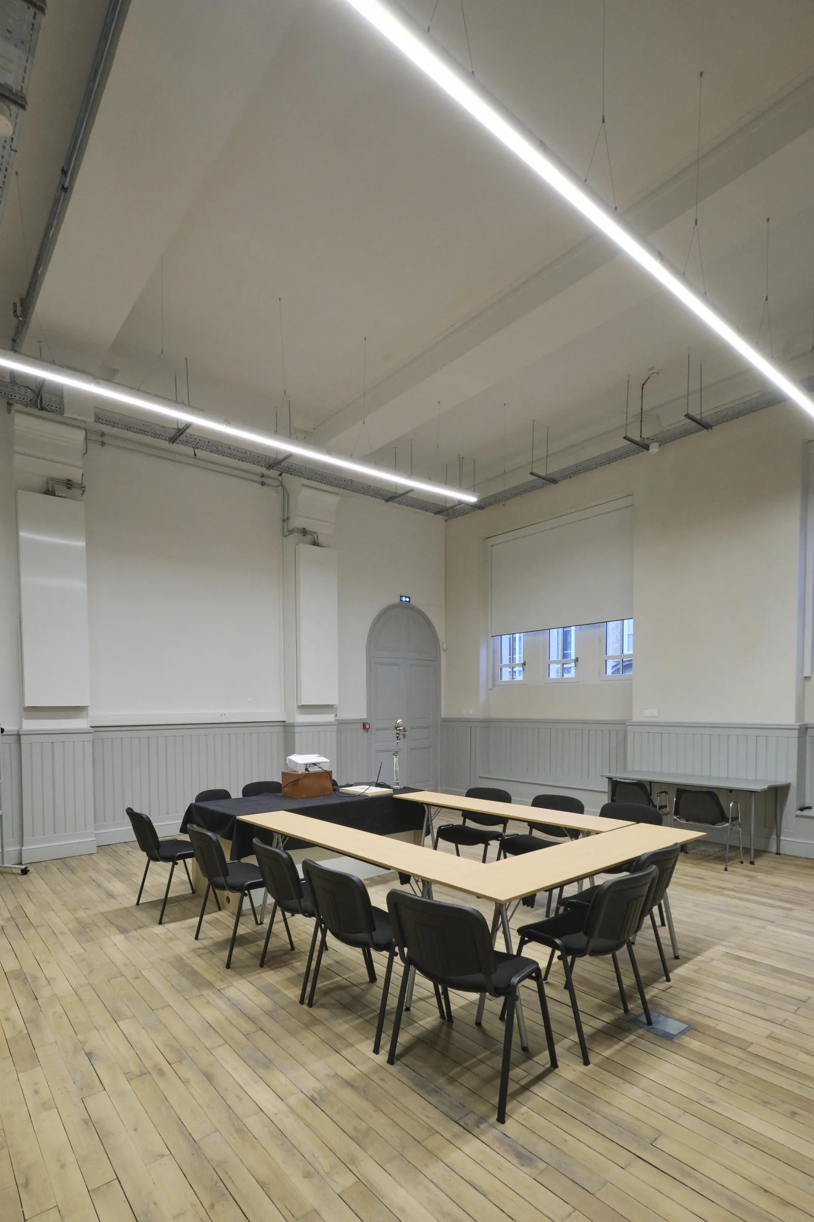 Salle de réunion moderne à la ManuCo Bordeaux avec table en U en bois, chaises noires, éclairage linéaire au plafond, tableau blanc et grandes fenêtres