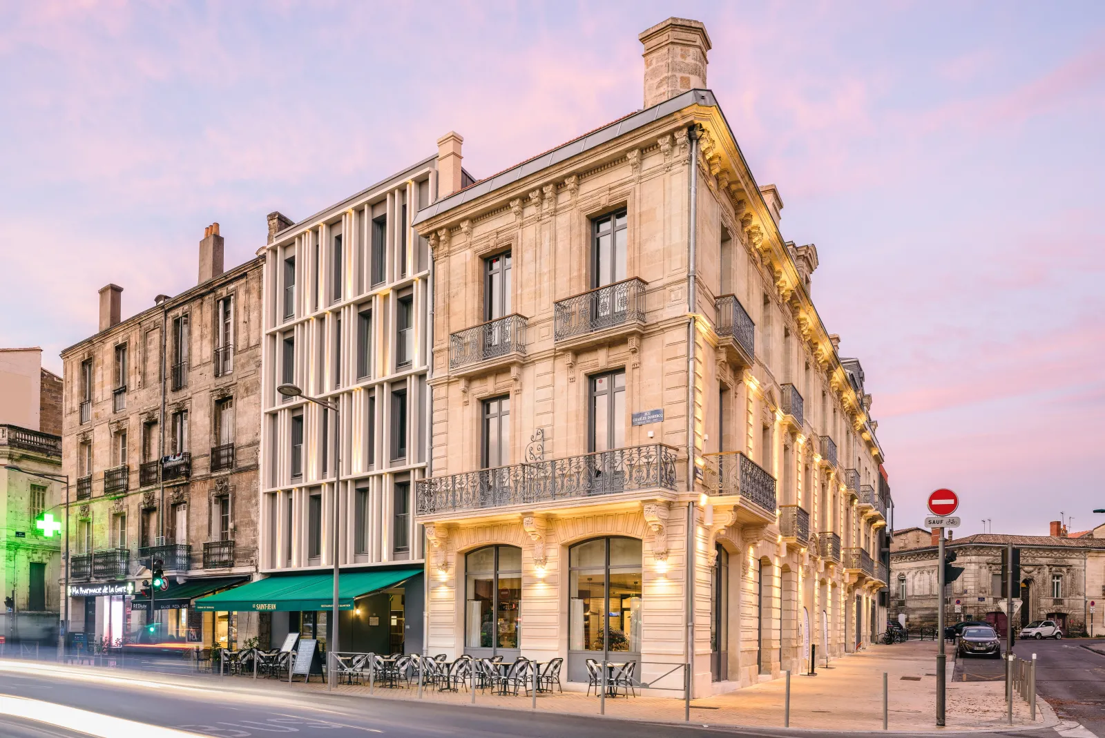 Hôtel Mercure Bordeaux Gare Atlantic, immeuble de pierre au façade crème, commerces au rez-de-chaussée et balcons en fer forgé, photographié au crépuscule dans le centre-ville de Bordeaux.