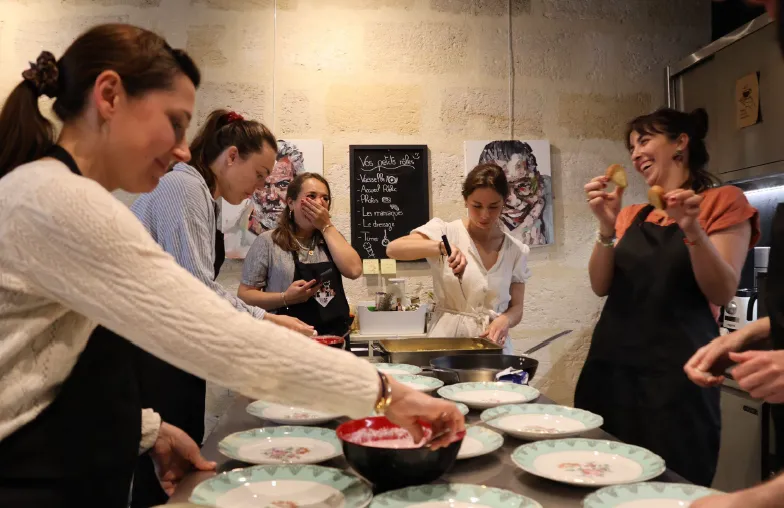 Un groupe de personnes participant à un cours de cuisine à La Cuisine de Camille à Bordeaux, avec des assiettes de nourriture sur le comptoir et une instructrice démontrant les techniques culinaires.