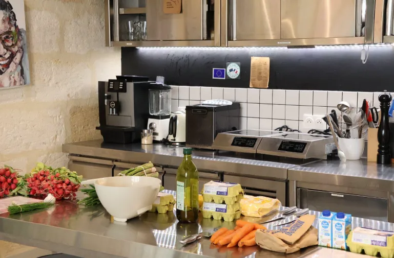 Plan de travail de cuisine moderne avec des provisions fraîches incluant des tomates rouges, des carottes, des œufs, du beurre, de l'huile d'olive et du lait, appareils de cuisson en arrière-plan