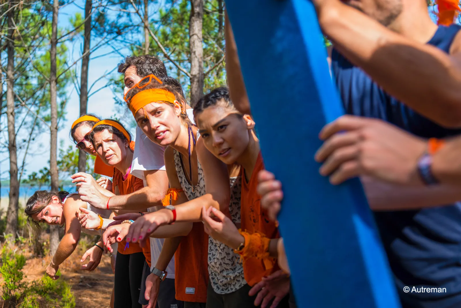Un groupe de personnes portant des bandeaux et bracelets orange se tiennent ensemble en plein air dans un cadre forestier, participant à une activité ou un événement de renforcement d'équipe.