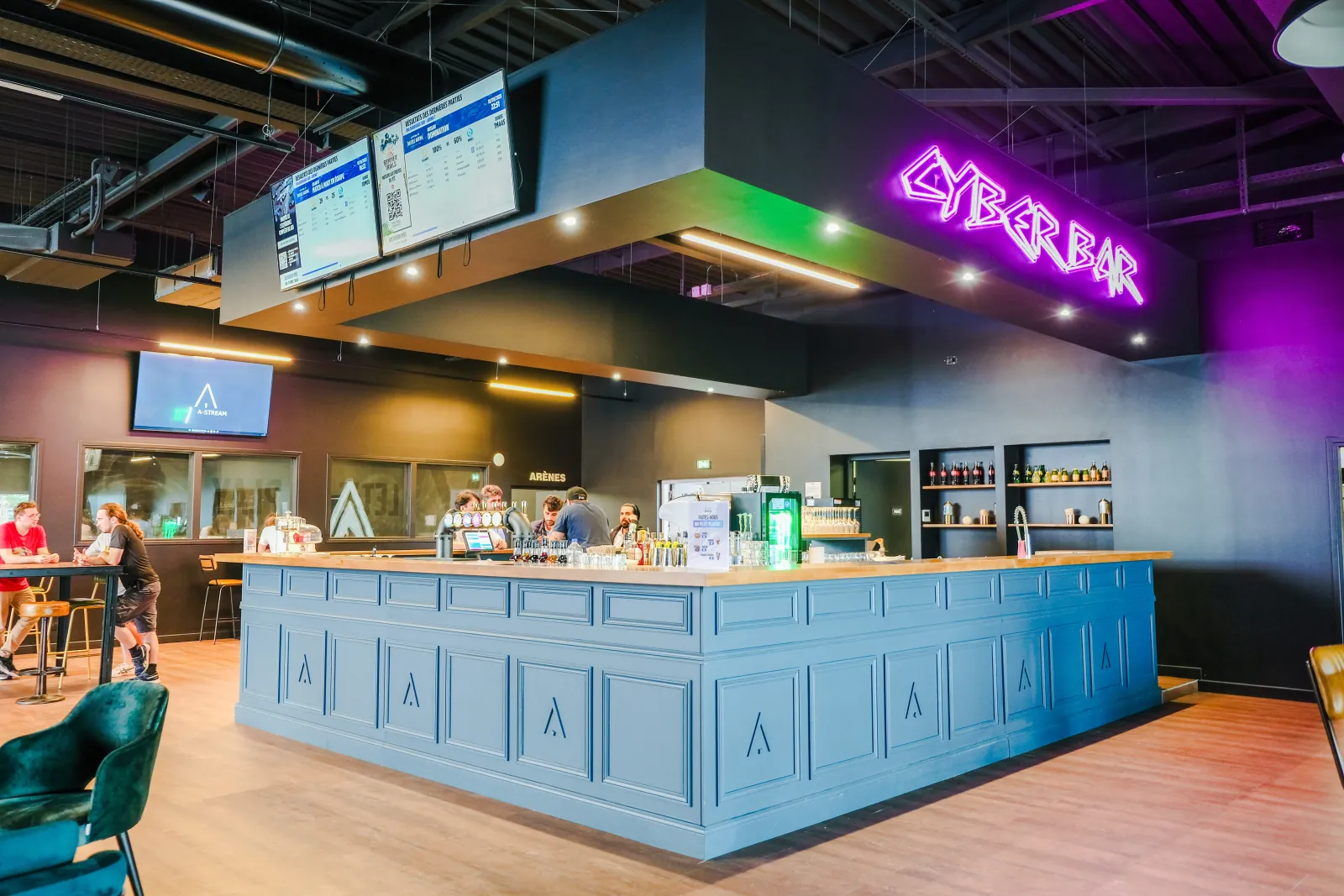 Intérieur moderne du cyber bar EVA Bordeaux Bègles avec comptoir bleu, enseigne néon violette, sol en bois, éclairage ambiant, personnel derrière le comptoir et écrans numériques