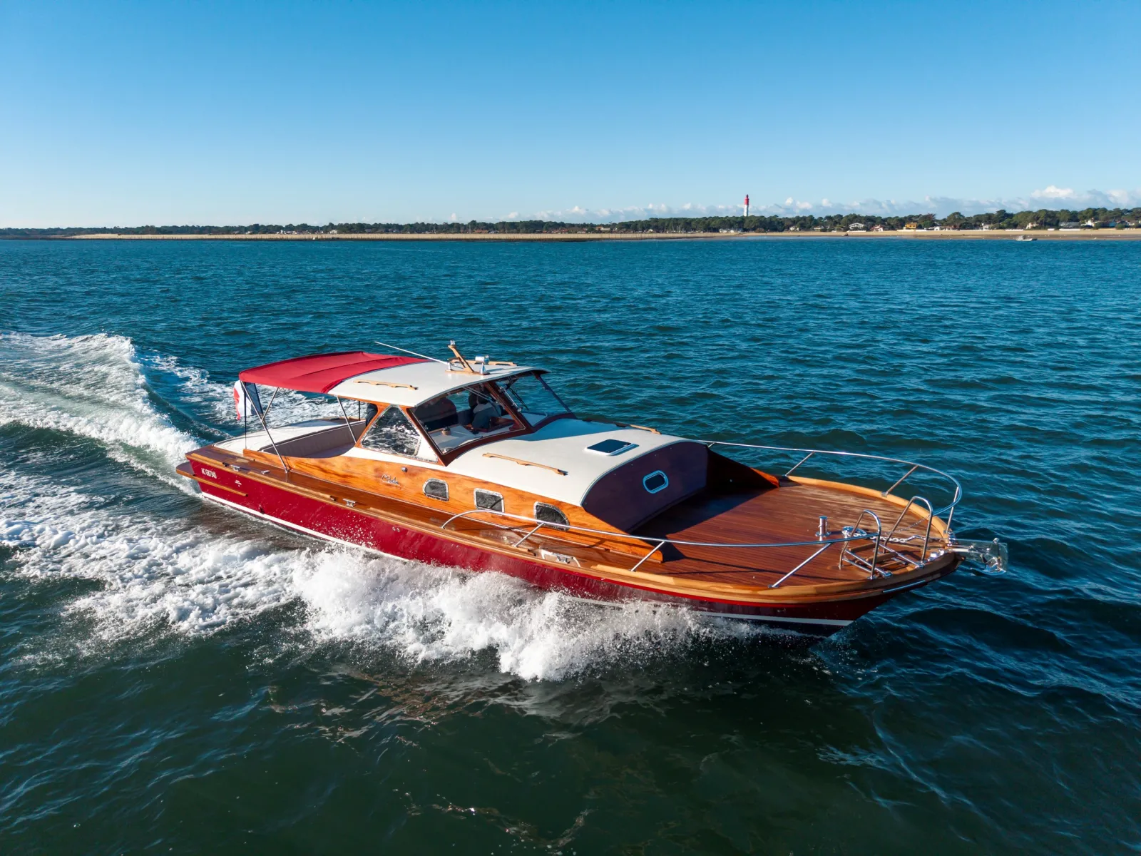 Un bateau à moteur en bois rouge et orange avec un auvent rouge mouillé dans les eaux peu profondes près d'une plage de sable fin par ciel bleu dégagé