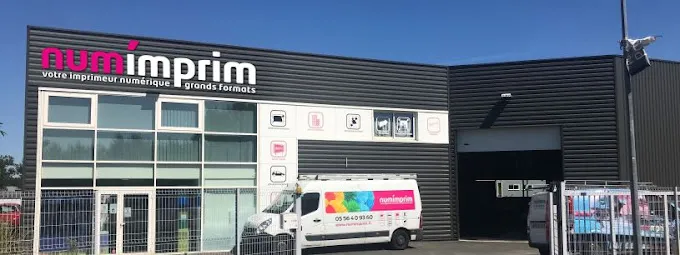 Façade du magasin NumImprim à Bordeaux avec bâtiment moderne, vitrines d'exposition et véhicule de livraison aux couleurs de la marque