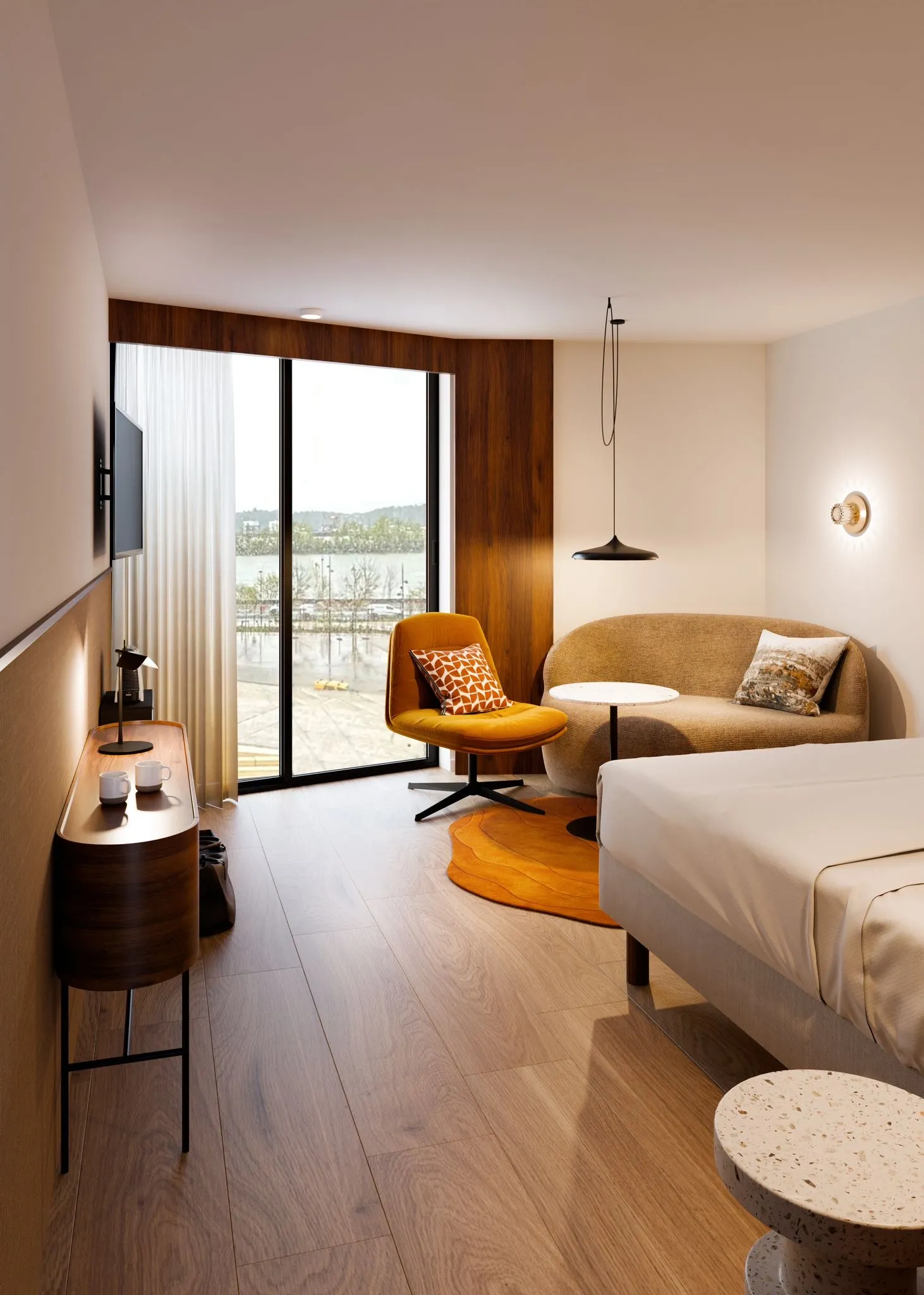 Chambre d'hôtel moderne à l'Hôtel 56 à Bordeaux avec lit, canapé beige, mur d'accent en bois, baies vitrées donnant sur un lac et mobilier contemporain avec éclairage chaleureux.