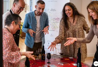 Cinq collègues réunis autour d'une table lors d'une dégustation de vin à Bordeaux, souriants et impliqués avec des verres de vin et des documents de dégustation, avec une carte régionale visible en arrière-plan.