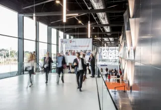 Participants en tenue professionnelle circulant dans un hall moderne de conférence avec de grandes baies vitrées donnant sur Bordeaux. Une bannière du 'Congrès Régions 2019' est visible, indiquant un congrès régional en cours.