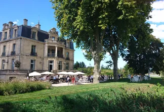 Un imposant château du 19e siècle à toiture mansardée accueillant un événement en plein air sous des parasols blancs dans un jardin paysagé avec des arbres centenaires, à Bordeaux.