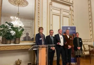 Groupe de six personnes debout à un pupitre dans une salle ornée avec des moulures dorées et un lustre, lors d'une cérémonie officielle ou d'une présentation à Bordeaux.