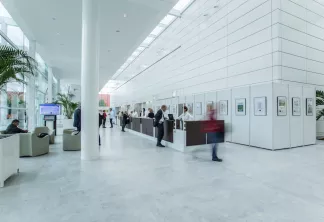 Intérieur moderne d'un bâtiment tertiaire à Bordeaux avec un vaste espace lumineux, puits de lumière, murs blancs ornés d'œuvres encadrées, plantes en pot, comptoir d'accueil et personnes circulant dans le corridor.