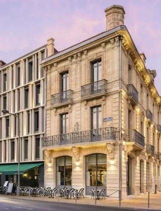 Immeuble de style haussmannien à Bordeaux avec façade en pierre de couleur crème, balcons ornementés et commerces au rez-de-chaussée, photographié au crépuscule sous un ciel violet