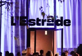 Vue extérieure du soir du lieu L'Estrade à Bordeaux avec des rideaux illuminés en violet et une foule de personnes rassemblées à l'entrée
