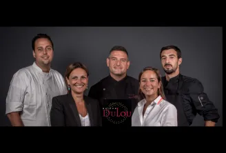 Cinq professionnels posant ensemble devant un fond gris, avec le logo de la Maison Dulou Traiteur visible sur le vêtement d'une personne.