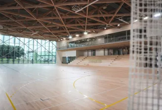 Intérieur d'un gymnase moderne de l'Université de Bordeaux avec un parquet sportif marqué, une structure de toit en acier apparente, de grandes baies vitrées, un niveau de galerie supérieure et des gradins en arrière-plan.