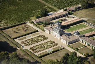Vue aérienne du Château de Malle à Bordeaux, montrant le manoir principal avec son dôme caractéristique, les jardins d'ornement formels aux motifs géométriques, les pelouses, les vignobles environnants et les bâtiments d'exploitation.