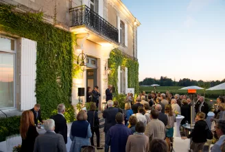 Réception élégante en soirée dans un domaine historique de Bordeaux avec façade couverte de lierre, invités discutant sur la terrasse, jardins entretenus visibles en arrière-plan au crépuscule.