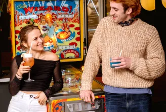 Deux personnes savourant des boissons à côté d'une machine de jeu d'arcade colorée et vintage dans un lieu moderne aux ambiances chaleureuses