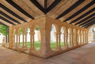 Cloître roman médiéval avec colonnes en pierre et arcades cintrées sous un plafond en bois moderne, illustrant l'architecture historique de Saint-Emilion.