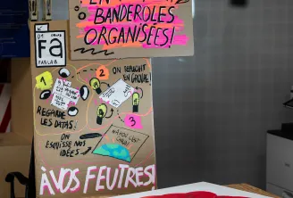 Une affiche artisanale sur une table en bois à Cap Sciences à Bordeaux présentant du texte français sur les banderoles organisées et les feuilles, avec des dessins colorés et des croquis, entourée de matériel de création et d'affichages éducatifs.