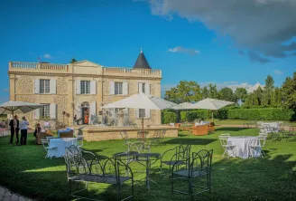Mise en place élégante d'un événement en plein air au Château Lafitte à Bordeaux, avec un manoir en pierre à tourelle, pelouse paysagée, parasols blancs et tables décorées aux nappes bleues et blanches.