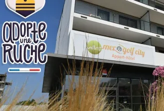 Devanture du Mer & Golf City Apart-Hôtel à Bordeaux avec le logo 'Adore une Ruche' à gauche, façade moderne du bâtiment avec balcons et herbes décoratives au premier plan