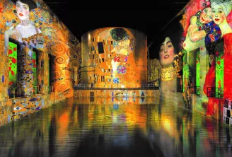 Installation d'art numérique immersif présentant les peintures emblématiques de Gustav Klimt projetées sur des murs cylindriques avec sol réfléchissant, mettant en avant 'Le Baiser' et des portraits en or, rouge et vert vibrants