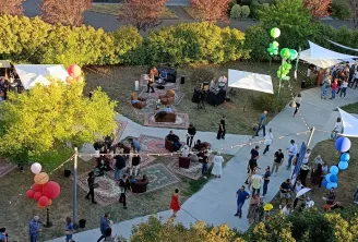 Vue aérienne d'un événement estival en plein air au Pullman Bordeaux Lac montrant des invités dans une cour paysagée avec arbustes à fleurs jaunes, ballons de décoration, chapiteaux blancs et zones de repos, entourés d'arbres aux couleurs automnales et de