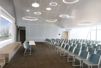 Salle de conférence moderne du Hilton Garden Inn Bordeaux avec des rangées de chaises vertes face à un écran de présentation, éclairage suspendu en forme d'anneaux et murs épurés.