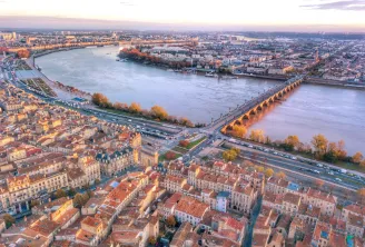 Vue aérienne de Bordeaux au coucher de soleil montrant la Garonne, le centre-ville historique avec ses toits en terre cuite, les ponts modernes et les quartiers environnants baignés dans la lumière dorée