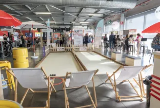 Terrain de pétanque couvert à Amexpo Sud Ouest à Bordeaux, avec des allées de sable blanc, des chaises en bois et des visiteurs explorant les stands dans un espace moderne.