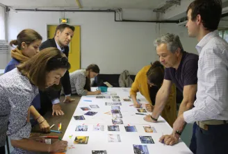 Un groupe de personnes réunies autour d'une table en train d'examiner et d'arranger des cartes et illustrations colorées liées au climat lors d'une activité collaborative d'atelier.