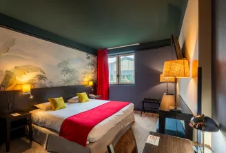 Chambre d'hôtel contemporaine avec lit double, chemin de lit rouge, coussins jaunes, tête de lit murale tropicale, éclairage chaleureux et vue sur la ville par fenêtre aux rideaux rouges