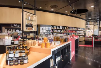 Intérieur de boutique moderne à la Cité du Vin à Bordeaux, présentant des étagères en bois, des produits de beauté et gastronomiques disposés sur des comptoirs blancs et orange, avec des accents roses et un éclairage contemporain.
