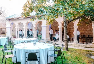 Événement en plein air dans une cour historique avec arcades voûtées, tables rondes avec nappes bleu clair, invités sous le feuillage automnal à Saint-Émilion