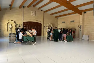 Groupe de visiteurs participant à une activité éducative autour du vin dans une grande salle moderne aux poutres en bois, murs en pierre et décoration de style médiéval au Fort Bioyard à Bordeaux.