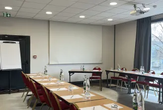 Salle de conférence moderne du Mercure Bordeaux Lac avec une longue table en bois, des chaises bordeaux, tableau blanc, projecteur et luminaires intégrés au plafond