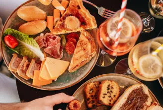 Deux personnes dégustant un brunch gastronomique avec charcuterie, viennoiseries, fruits frais et vin rosé sur une table noire lors d'une croisière sur la Garonne à Bordeaux