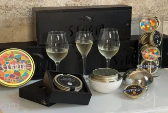 Ensemble de dégustation caviar et champagne de luxe Sturm présentant le caviar d'Aquitaine premium, trois verres de vin blanc, enseigne néon, assiettes décoratives et emballages de marque sur surface blanche