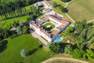 Vue aérienne du Château Toulouse-Lautrec, un château blanc historique aux toitures de tuiles terracotta, entouré de jardins aménagés, piscine et campagne verdoyante près de Bordeaux.