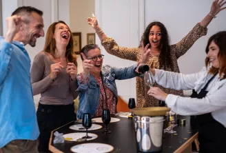 Un groupe de cinq personnes riant et célébrant ensemble autour d'une table avec des verres de vin et des couverts lors d'une dégustation au Casino du Vin by Invino Event à Bordeaux.